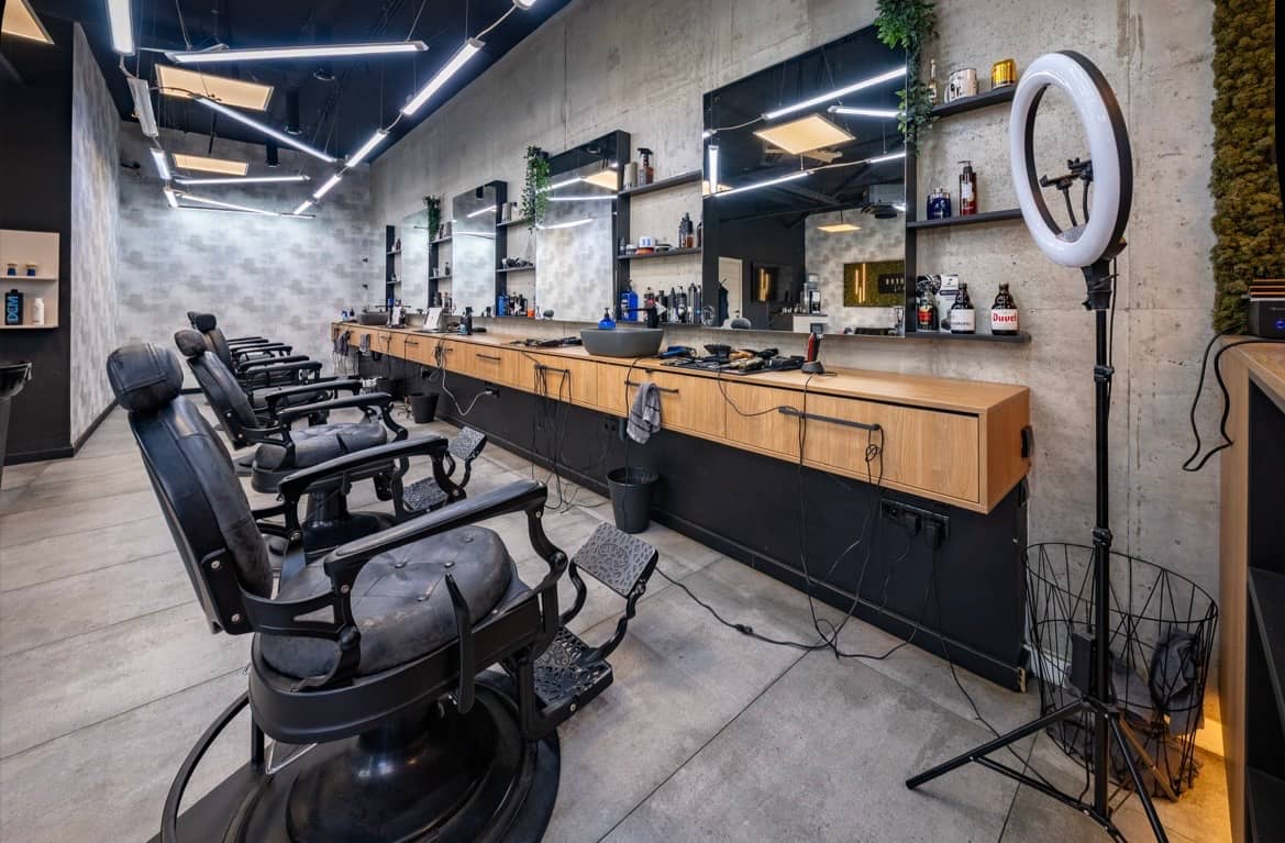 A row of barber chairs at the oak counter, with mirrors and linear LED lighting above