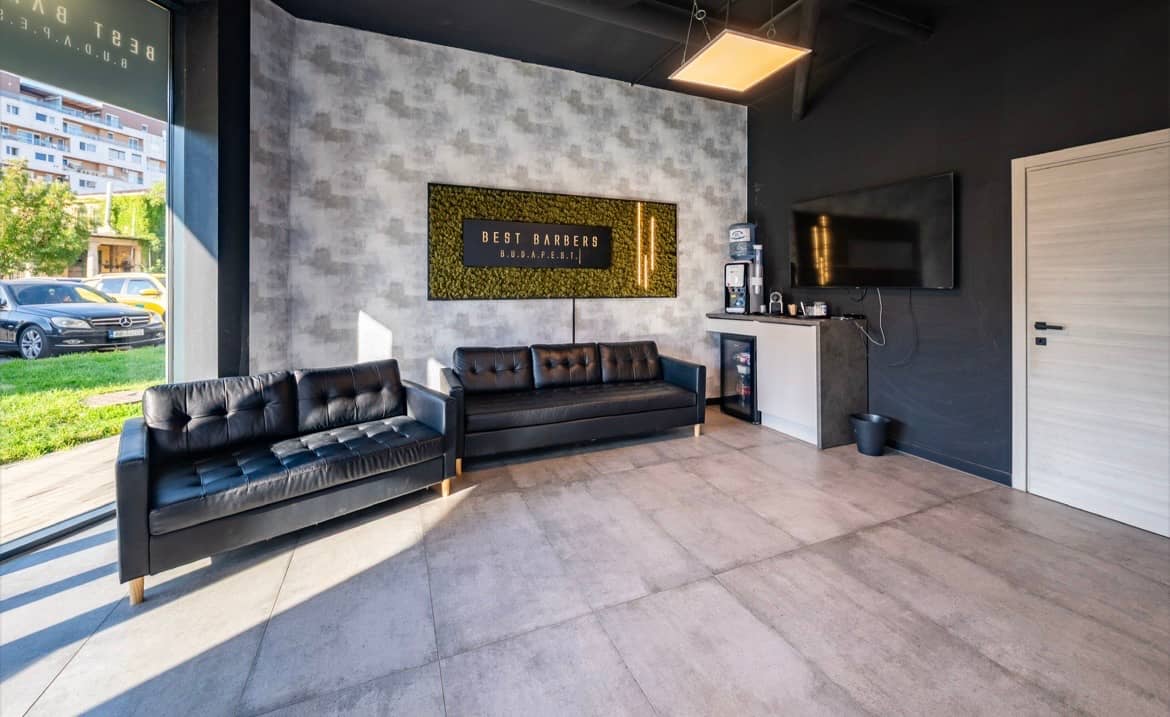 The waiting area: black leather sofas, a living moss panel with the Best Barbers sign, and a coffee machine